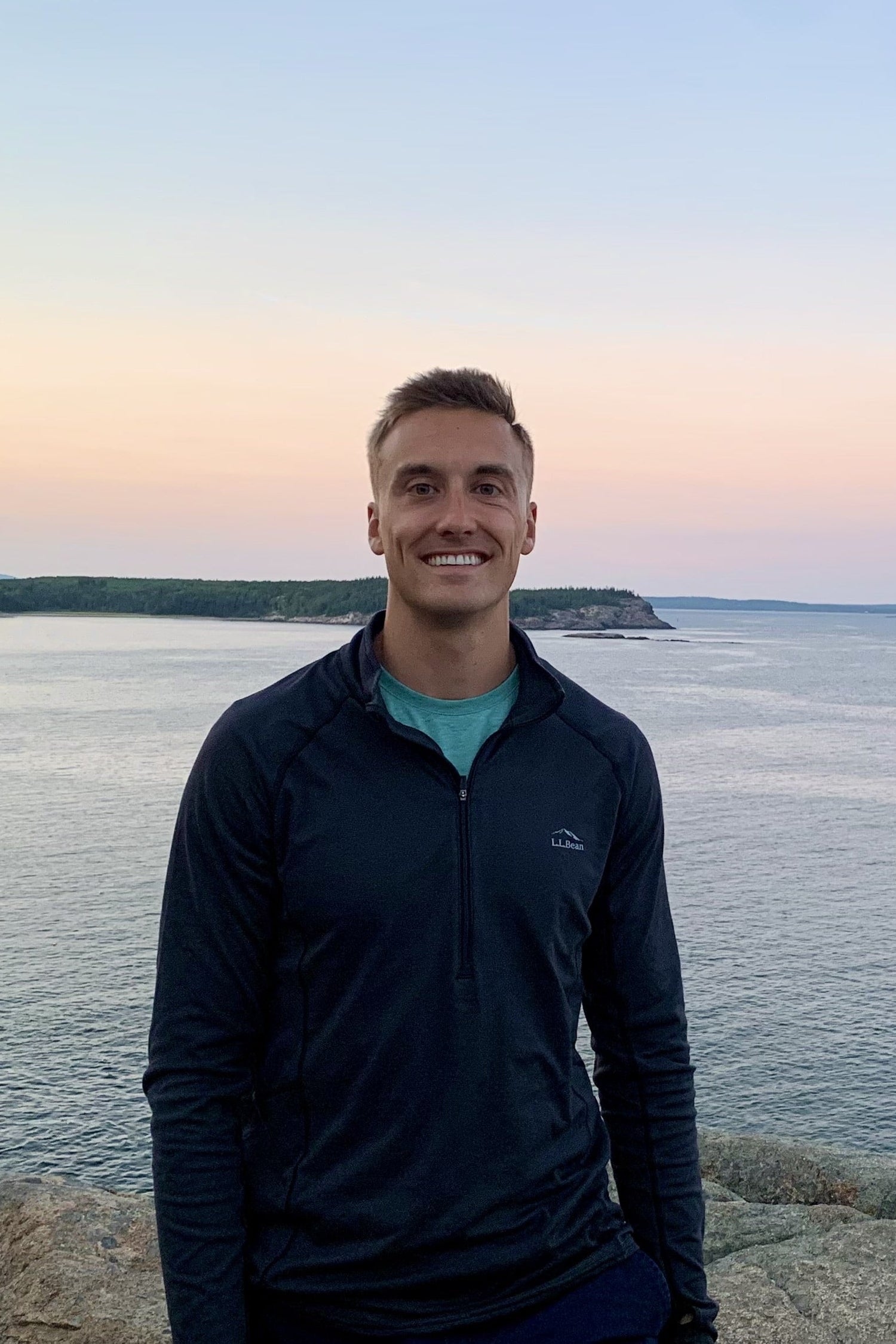 Person standing on a rocky outcrop by a body of water at sunset