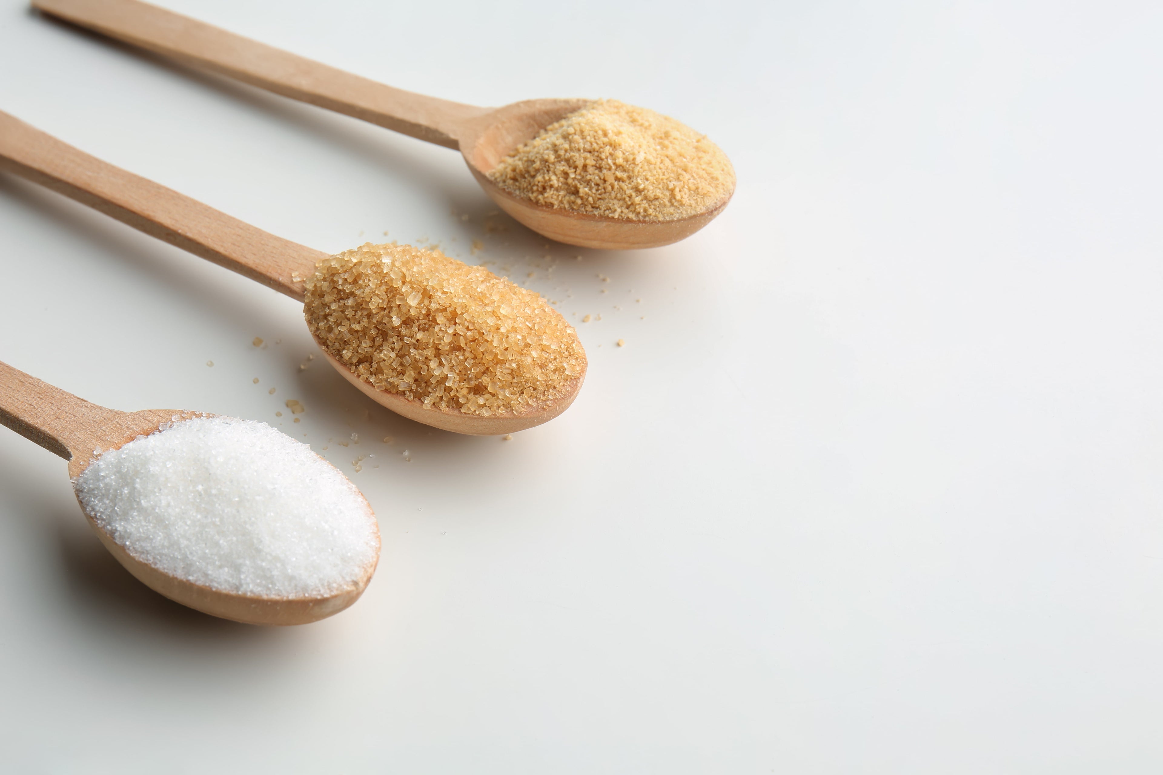 Three wooden spoons with different types of sugar on a light background